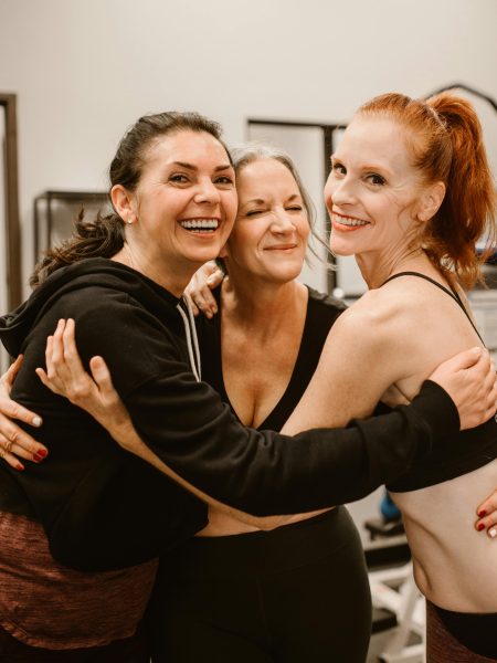 Three happy women hugging at the gym, celebrating friendship and wellness.